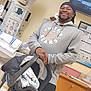 man, baby_car_seat, hospital_room, medical_equipment, smiling, hoodie, furniture, cabinet, monitor, television, glasses, newborn, blanket, person, indoors, light, floor, wall, hand, carrying