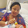woman, baby, hospital_bed, feeding, bottle, blanket, hat, smile, hospital_room, medical_tube, tattoo, wristband, nail_polish, person, bed, pillow, furniture, indoor, care, newborn