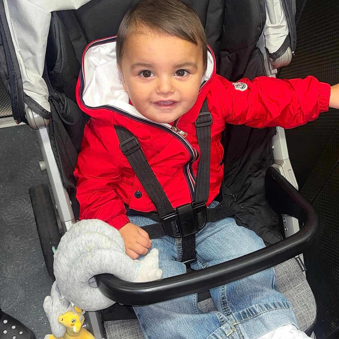 Kayaan is registered to the contest to win money with this photo: baby, black_stroller, casual_clothing, child, cute, floor, happy, indoor, jeans, person, playful, portrait, red_jacket, seatbelt, smile, stroller, toddler, toy, white_shoes, young_child