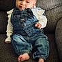 Autumn is registered to the contest to win money with this photo: baby, child, denim_overalls, white_sweater, couch, gray_fabric, foot, hand, face, portrait, indoor, infant, seated, cute, expression, clothing, young_child, skin, eyes, casual