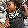 Jashawn is registered to the contest to win money with this photo: baby, infant, child, clothing, tshirt, text, bedspread, pattern, blue_pants, sports_theme, football, basketball, baseball, person, skin, hand, face, curious, lying_down, natural_light