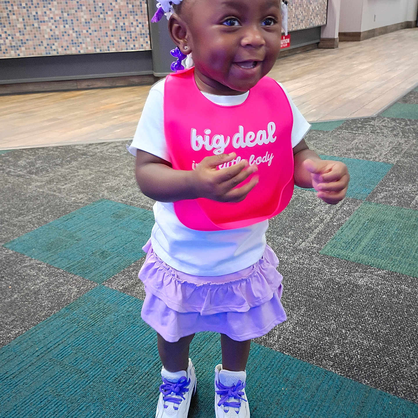 Imani joined the competition — help win amazing prizes! braids, carpet, child, clothing, counter, cute, floor_tiles, happy, indoor, lilac_skirt, person, pink_bib, public_space, purple_beads, purple_laces, smiling, sneakers, standing, toddler, white_shirt