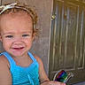 child, toddler, smiling, portrait, outdoor, doorway, front_door, wall, curly_hair, hair_bow, blue_clothing, tank_top, sunglasses, rainbow_lenses, hand, fashion, happy, face, standing, daylight