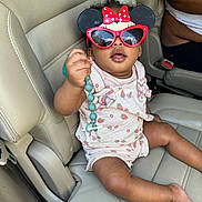 Brooklyn is registered to the contest to win money with this photo: baby, child, sunglasses, minnie_mouse, car_seat, pacifier_clip, beads, clothing, person, infant, seat, leather, interior, hand, cute, accessory, pink, white, toy, car