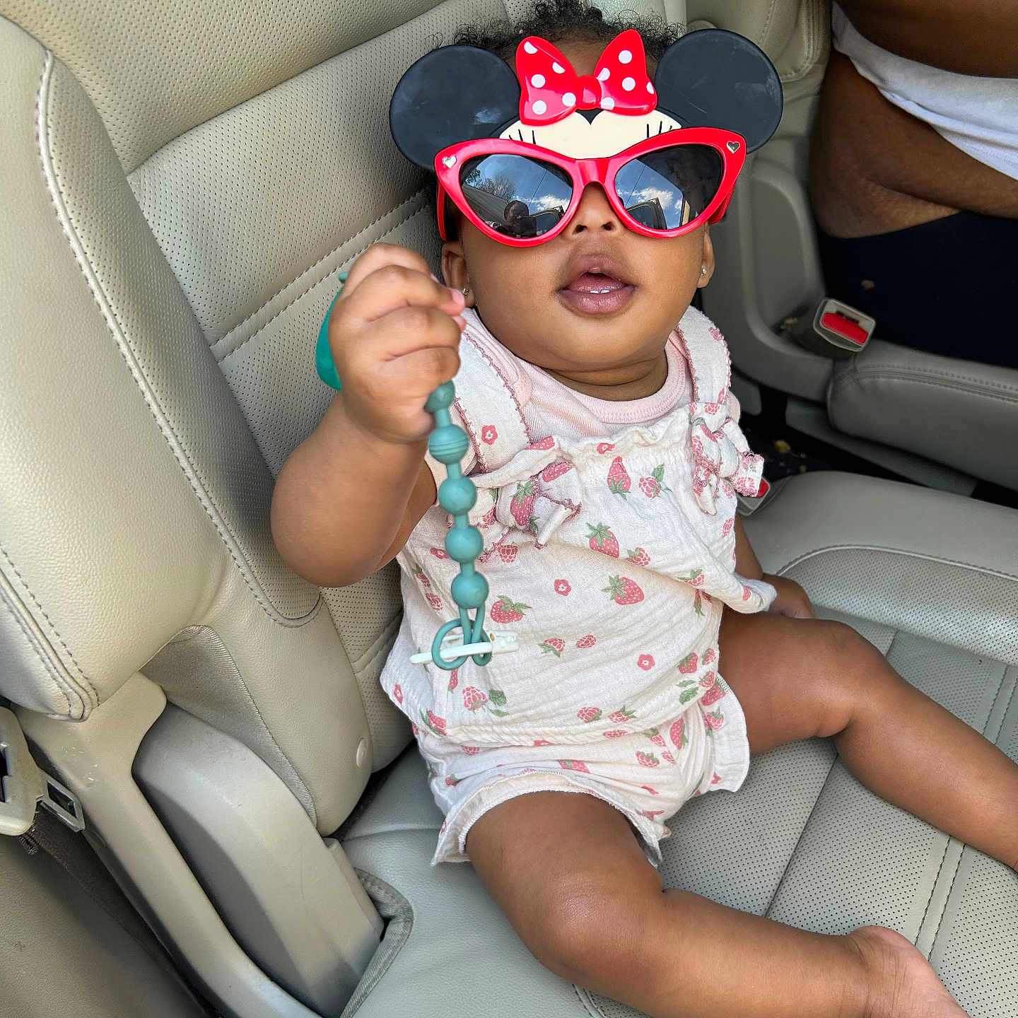 Brooklyn is registered to the contest to win money with this photo: baby, child, sunglasses, minnie_mouse, car_seat, pacifier_clip, beads, clothing, person, infant, seat, leather, interior, hand, cute, accessory, pink, white, toy, car