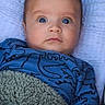 Christopher is registered to the contest to win money with this photo: baby, bedding, blanket, blue_clothing, brown_hair, child, close_up, cozy, face, happy, head, indoors, infant, looking_at_camera, lying_down, onesie, photography, portrait, textile, wide_eyes