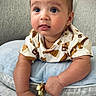 baby, blanket, blue_eyes, brown_hair, child, close_up, couch, gold_toy, indoor, infant, onesie, patterned_clothing, pillow, portrait, sitting, smiling, soft_lighting, tongue_out, toy, wide_eyes
