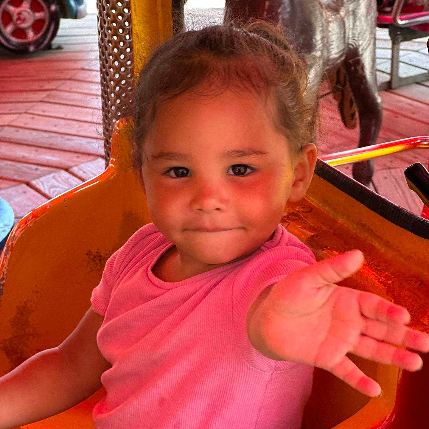 Haïly participe au concours pour gagner de l'argent avec cette photo : amusement_ride, child, colorful, cute, daylight, expression, face, fun, hair_tied, hand_reaching, orange_seat, outdoor, park, person, pink_shirt, playful, seatbelt, smiling, toddler, wooden_floor