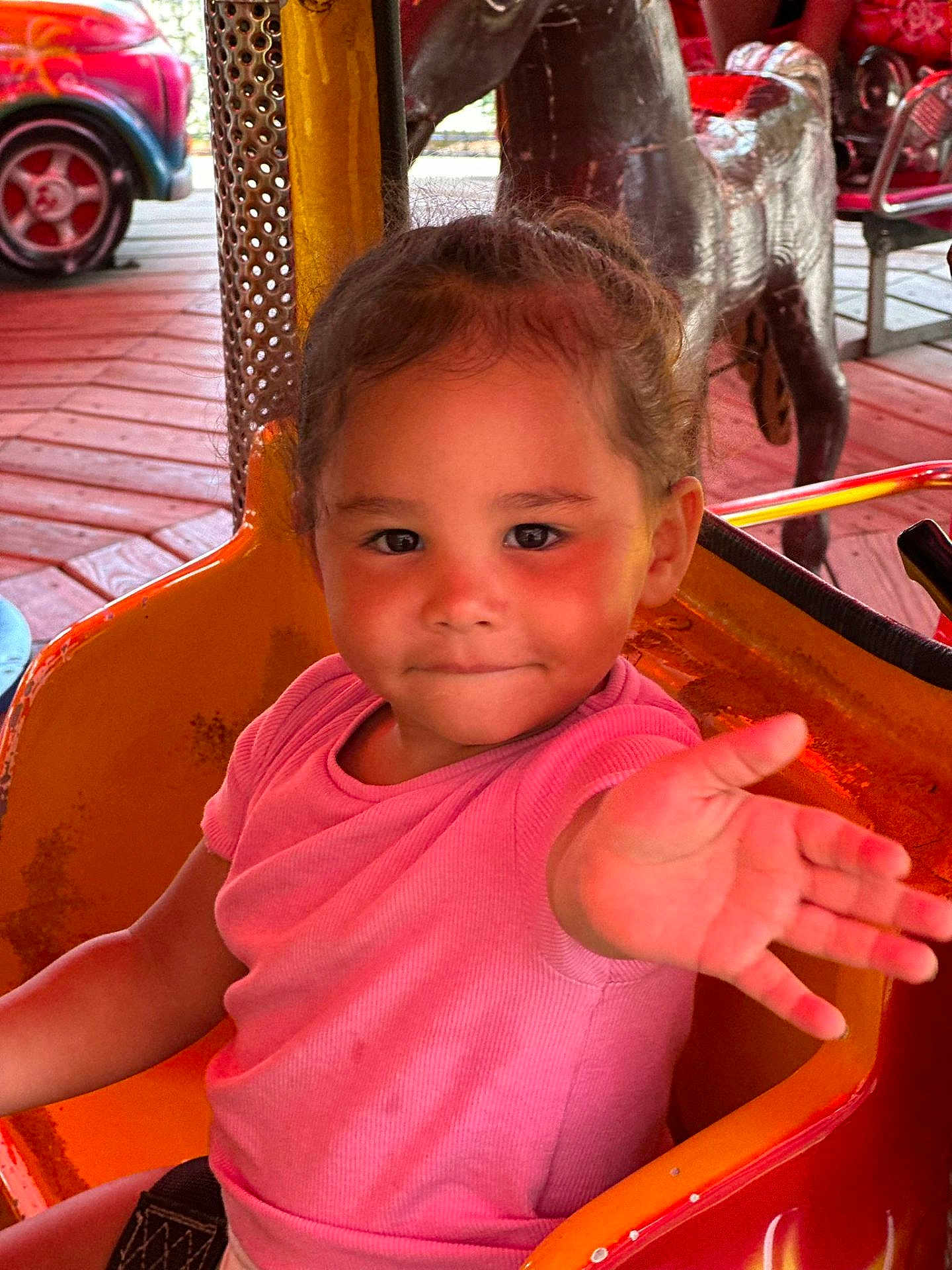 Haïly participe au concours pour gagner de l'argent avec cette photo : amusement_ride, child, colorful, cute, daylight, expression, face, fun, hair_tied, hand_reaching, orange_seat, outdoor, park, person, pink_shirt, playful, seatbelt, smiling, toddler, wooden_floor