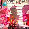 child, birthday, cake, candles, gift_bags, pink_crown, smiling, window_blinds, table, chocolate_cake, number_4_candle, party, celebration, indoors, present, girl, happy, food, dessert, lighting