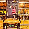 Promiss is registered to the contest to win money with this photo: child, smiling, chair, oversized, restaurant, indoor, decorative, sign, text, window, table, floor, lighting, person, clothing, sandals, curly_hair, bag, stop_sign, background