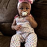 baby, infant, child, portrait, sitting, couch, pacifier, headband, pink_bow, patterned_clothing, onesie, smiling, indoor, living_room, furniture, brown_couch, close_up, adorable, hands, feet