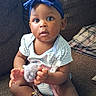Egypt is registered to the contest to win money with this photo: baby, barefoot, blue, bow, brown_skin, child, couch, curious, cushion, headband, indoor, infant, living_room, looking_at_camera, pacifier, plush_toy, portrait, sitting, striped_clothing, toy