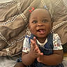 adorable, baby, bed, bedroom, child, clapping, close_up, denim_overalls, eyes, face, floral_shirt, hair_bows, happy, indoors, infant, pillows, portrait, sitting, smiling, sunlight