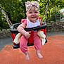 baby, barefoot, blanket, bow, chains, child, greenery, happy, headband, infant, outdoor, park, pink_clothing, playground, seat, smiling, stone_wall, sunlight, swing, trees