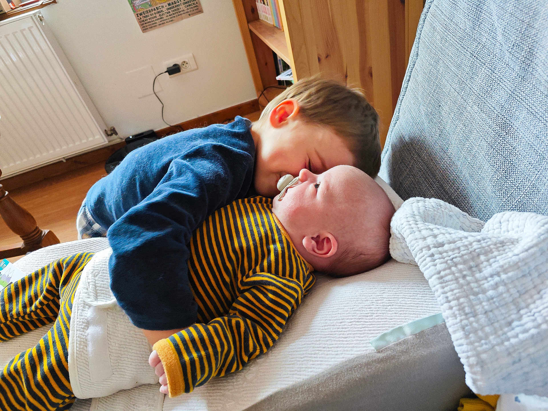 Milo participe au concours pour gagner de l'argent avec cette photo : baby, toddler, child, couch, blanket, pacifier, striped_clothing, blue_sweater, indoor, wooden_floor, bookshelf, radiator, closeup, family, love, hug, furniture, home, face, person