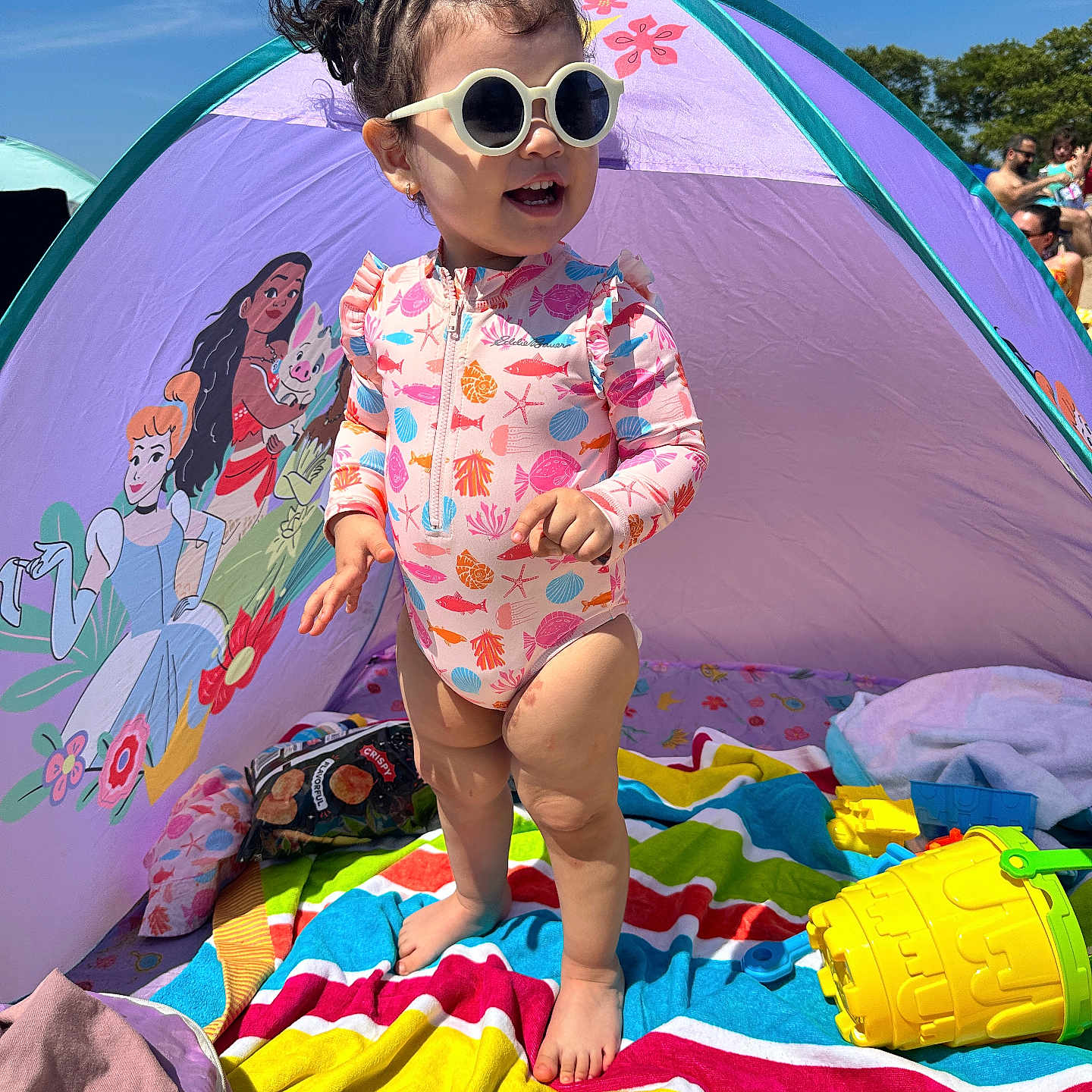 Itzel is registered to the contest to win money with this photo: barefoot, beach_tent, cartoon, child, colorful, daylight, happy, outdoor, playing, princess, purple, sand, striped_towel, summer, sunglasses, sunny, swimsuit, toddler, toy, yellow