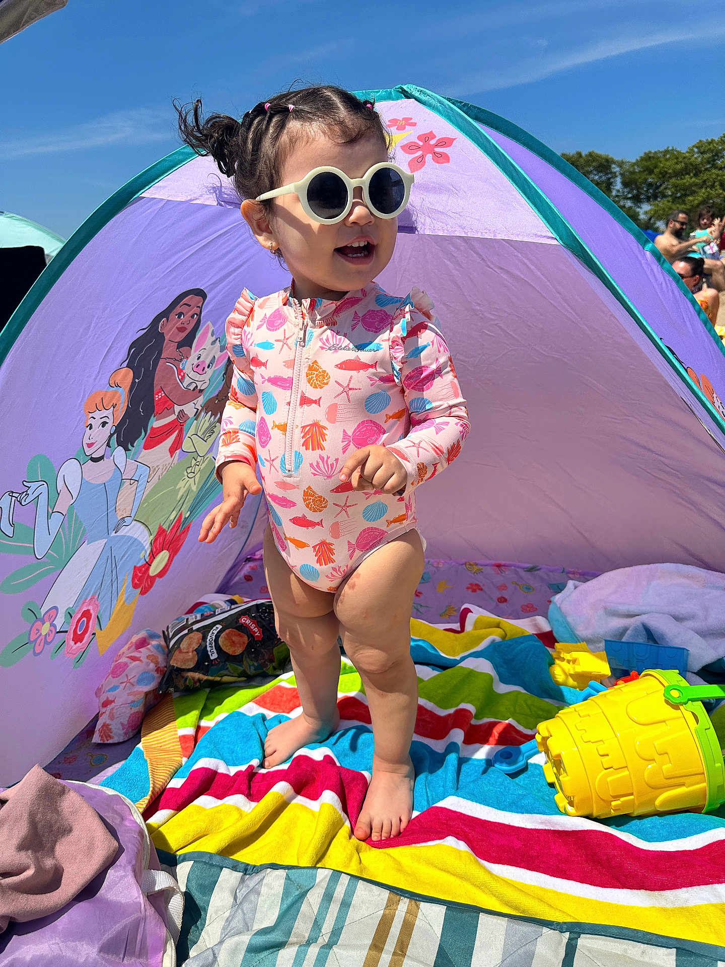 Itzel is registered to the contest to win money with this photo: barefoot, beach_tent, cartoon, child, colorful, daylight, happy, outdoor, playing, princess, purple, sand, striped_towel, summer, sunglasses, sunny, swimsuit, toddler, toy, yellow