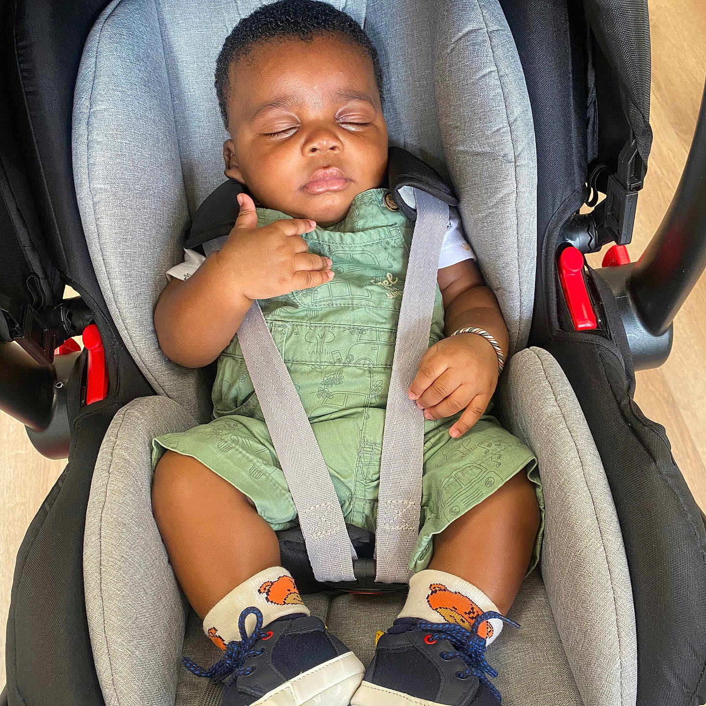 Soualiho a rejoint le concours — aidez-le/la à gagner de superbes lots ! baby, black_hair, bracelet, car_seat, child, closed_eyes, comfort, cute, floor, green_overalls, indoor, infant, infant_clothing, peaceful, resting, seatbelt, shoes, sleeping, socks, toddler