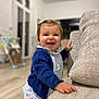 toddler, child, smiling, indoor, couch, blue_sweater, white_shirt, hair_clip, happy, standing, furniture, living_room, flooring, window, toy, baby, person, home, cute, portrait