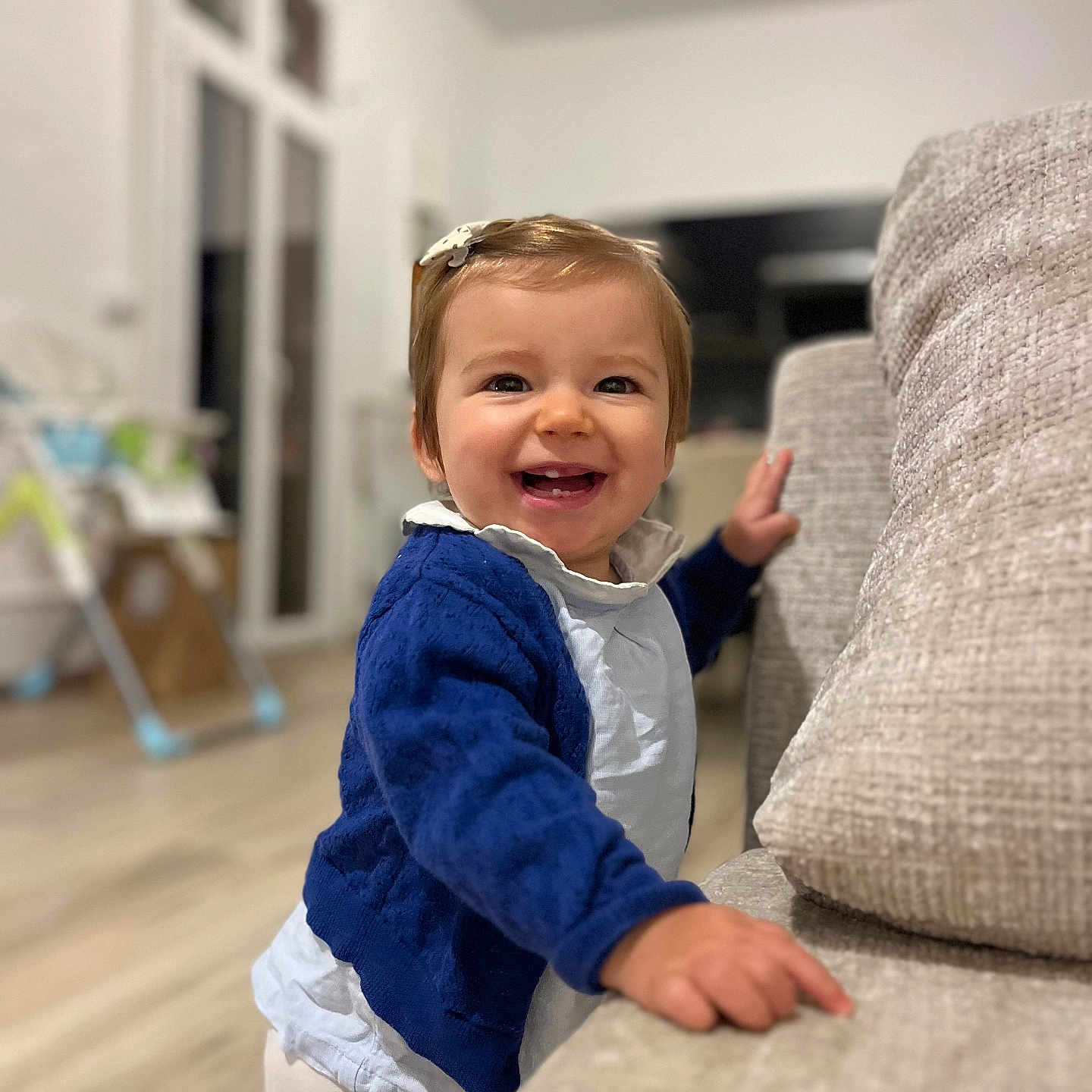 Swann participe au concours pour gagner de l'argent avec cette photo : baby, blue_sweater, child, couch, cute, flooring, furniture, hair_clip, happy, home, indoor, living_room, person, portrait, smiling, standing, toddler, toy, white_shirt, window