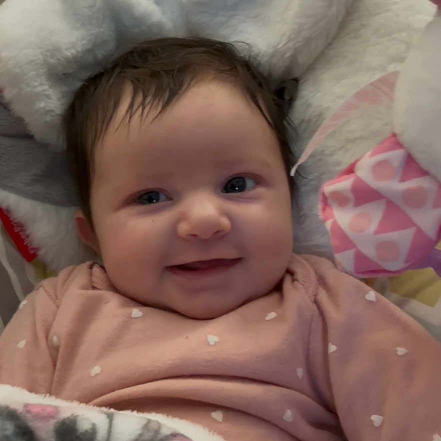 Rayvn joined the competition — help win amazing prizes! baby, infant, child, smiling, portrait, face, eyes, indoors, blanket, plush_toy, stuffed_animal, bedding, crib, pink_clothing, heart_pattern, cozy, happy, sitting, closeup, photography