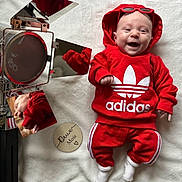 Maëlan a rejoint le concours — aidez-le/la à gagner de superbes lots ! adidas, baby, baby_fashion, casual_outfit, cute, handwritten_text, happy, hoodie, indoor, infant, lying_down, portrait, red_clothing, reflection, smiling, soft_texture, spotlight, sunglasses, white_blanket, wooden_sign