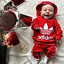 adidas, baby, baby_fashion, casual_outfit, cute, handwritten_text, happy, hoodie, indoor, infant, lying_down, portrait, red_clothing, reflection, smiling, soft_texture, spotlight, sunglasses, white_blanket, wooden_sign
