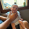 baby, infant, child, smiling, portrait, sitting, indoors, window, adult, hands, lap, onesie, barefoot, couch, sunlight, car, drink_can, windowsill, home, happy