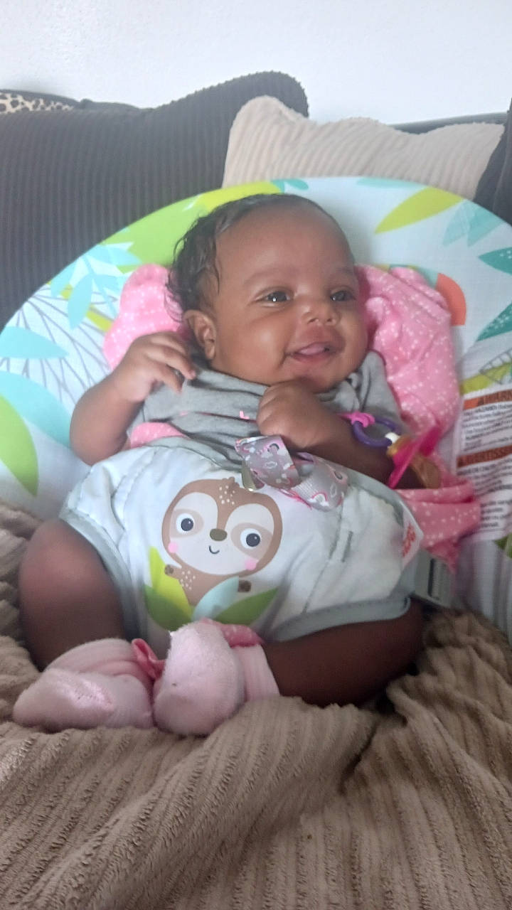 Marley is registered to the contest to win money with this photo: baby, baby_toddler_clothing, cheek, child, comfort, eye, facial_expression, fun, hairstyle, head, human_body, infant_bed, lap, linens, mouth, person, pink, skin, smile, toddler