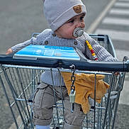 Kayron a rejoint le concours — aidez-le/la à gagner de superbes lots ! toddler, child, shopping_cart, pacifier, knit_hat, sweater, plush_toy, sneakers, pants, outdoor, street, crosswalk, curious, baby, clothing, person, toy, casual, daylight, urban