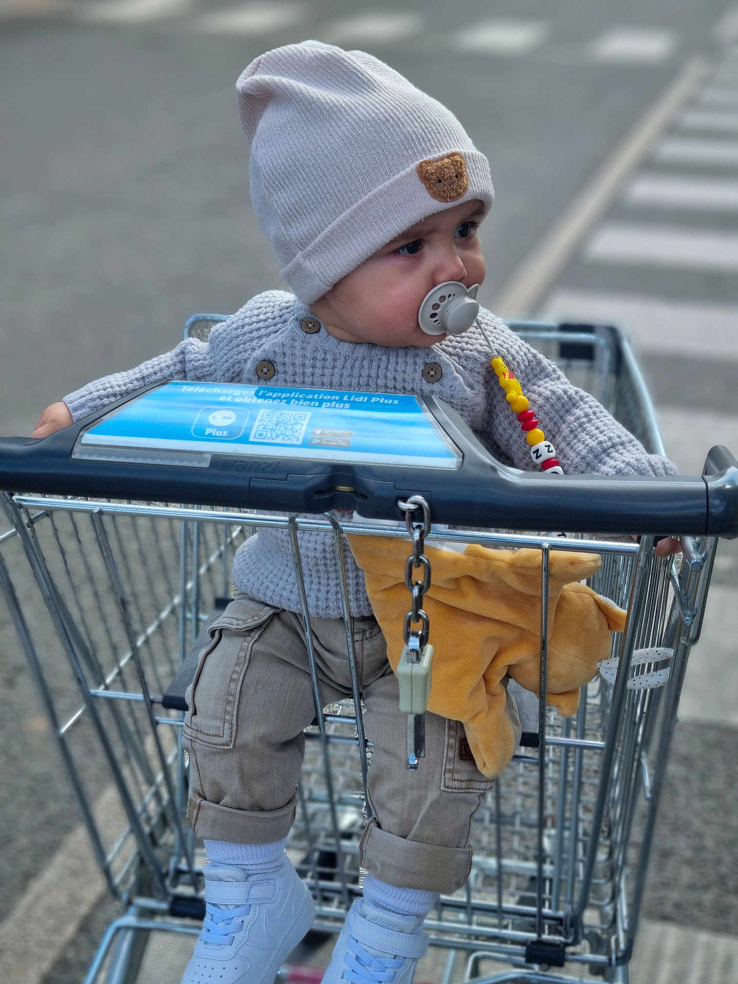 Kayron a rejoint le concours — aidez-le/la à gagner de superbes lots ! toddler, child, shopping_cart, pacifier, knit_hat, sweater, plush_toy, sneakers, pants, outdoor, street, crosswalk, curious, baby, clothing, person, toy, casual, daylight, urban