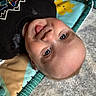 Patrick joined the competition — help win amazing prizes! baby, child, tongue_out, blue_eyes, play_mat, black_shirt, face, skin, expression, cute, infant, lying_down, curious, indoors, soft_texture, colorful, young_child, person, head, closeup