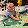 baby, child, play_mat, dinosaur, alphabet, plush_toy, yellow_star, smiling, indoor, living_room, couch, baby_swing, curious, joyful, toddler, clothing, head, hands, floor, toy