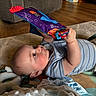 Patrick joined the competition — help win amazing prizes! baby, infant, child, toy, soft_book, colorful, play_mat, blanket, plush_toy, floor, wooden_floor, couch, blue_striped_shirt, indoor, curious, lying_down, hand, face, eyes, room