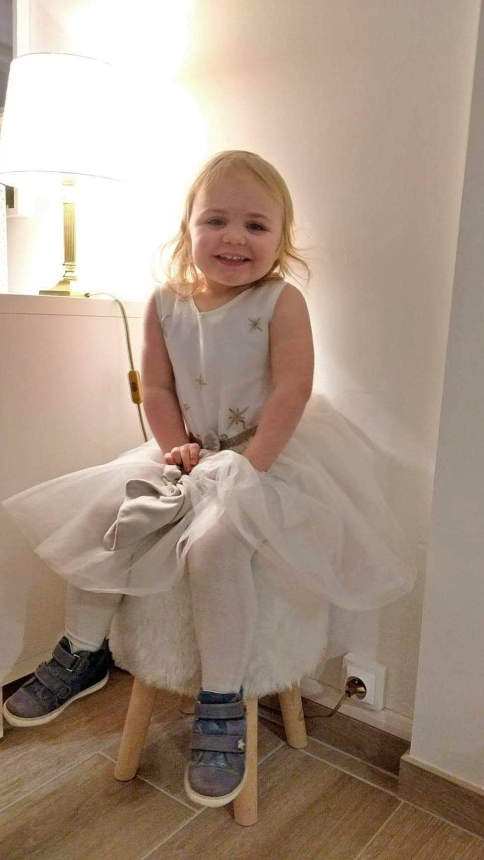 Nina participe au concours pour gagner de l'argent avec cette photo : bridal_party_dress, child, child_model, clothing, costume, dress, joy, leg, person, shoe, sitting, toddler, white