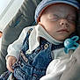 adorable, baby, baby_clothing, blue_cap, child, closeup, cushioned_seat, cute, denim_overalls, indoors, infant, pacifier, peaceful, portrait, relaxed, resting, sleeping, small_hands, soft_lighting, white_sweater
