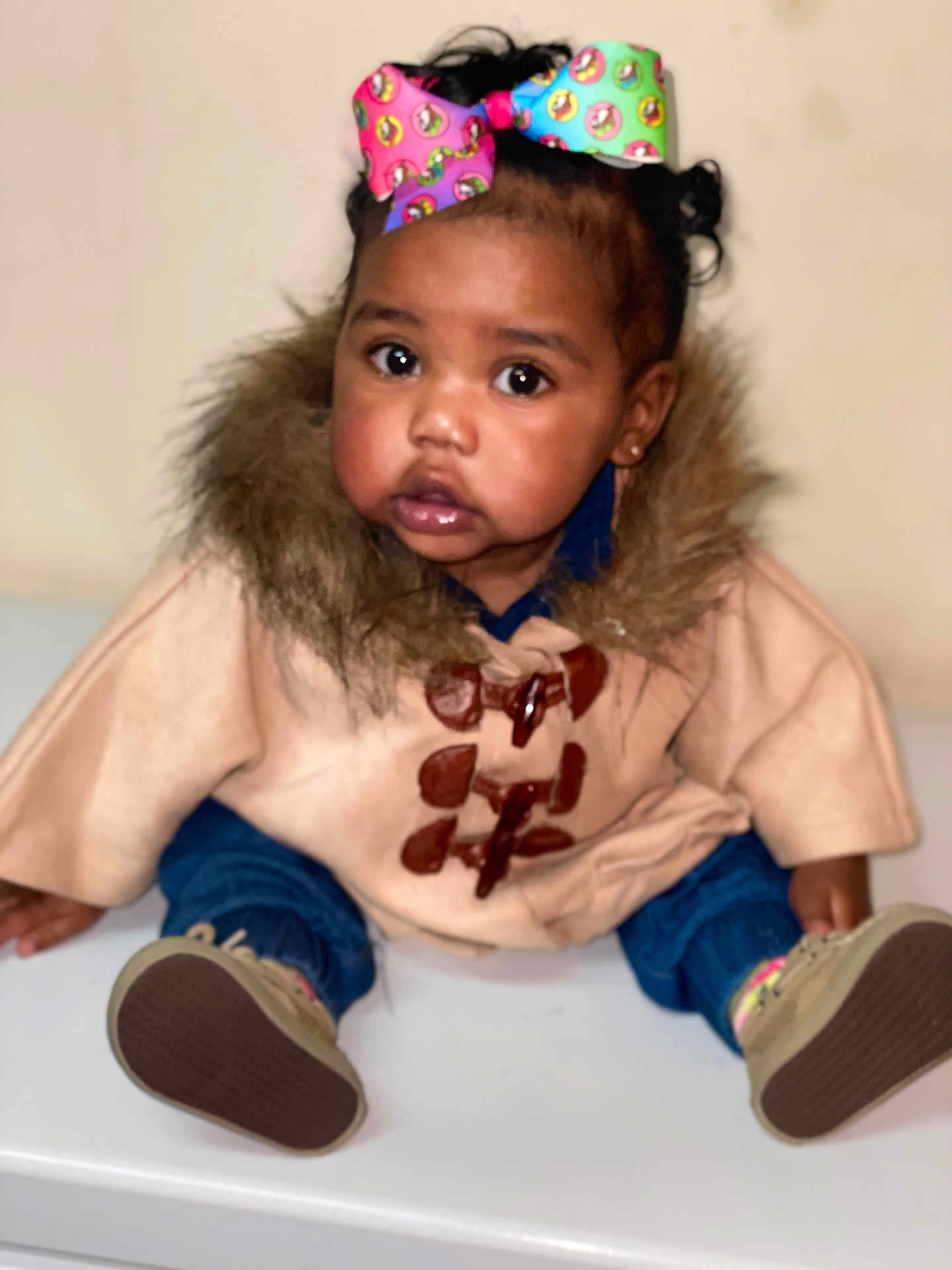 Maryleigh is registered to the contest to win money with this photo: baby, child, girl, coat, fur_trim, bow, colorful_bow, jeans, shoes, sitting, indoor, curly_hair, cute, portrait, face, eyes, expression, fashion, warm_clothing, adorable