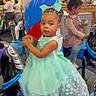 child, toddler, girl, dress, princess_dress, carousel, amusement_park, indoor, playground, smiling, portrait, braids, hair_bow, mint_green, seated, ride, colorful, family, entertainment, photograph