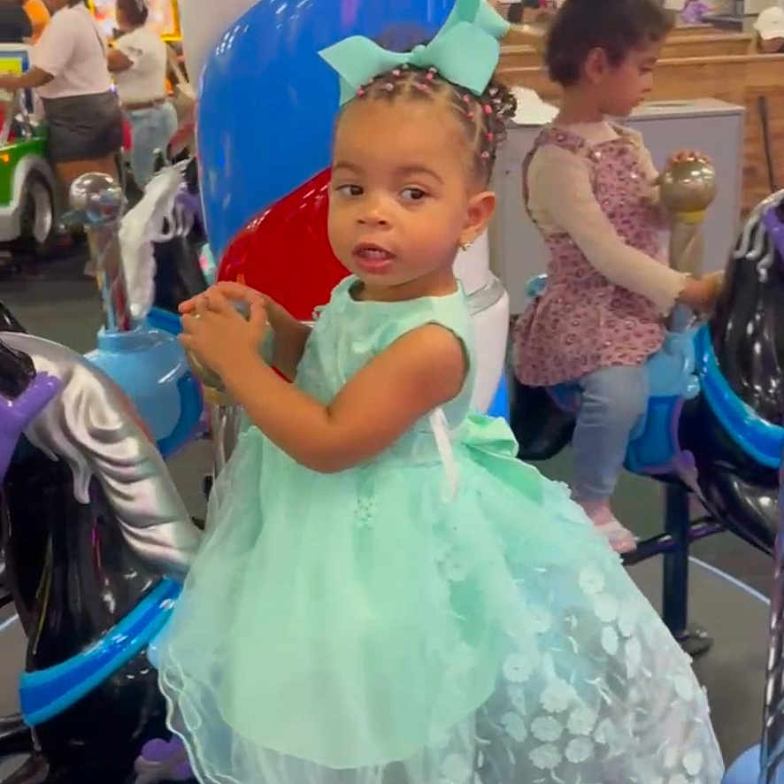 Dannylynn is registered to the contest to win money with this photo: child, toddler, girl, dress, princess_dress, carousel, amusement_park, indoor, playground, smiling, portrait, braids, hair_bow, mint_green, seated, ride, colorful, family, entertainment, photograph