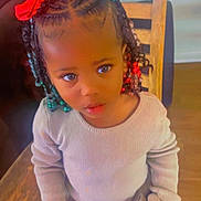 Taziyah joined the competition — help win amazing prizes! child, girl, braided_hair, hair_bows, red_bow, green_bow, sitting, wooden_chair, beige_sweater, patterned_pants, indoor, backpack, curious_expression, young_child, person, cute, fashion, portrait, home, floor