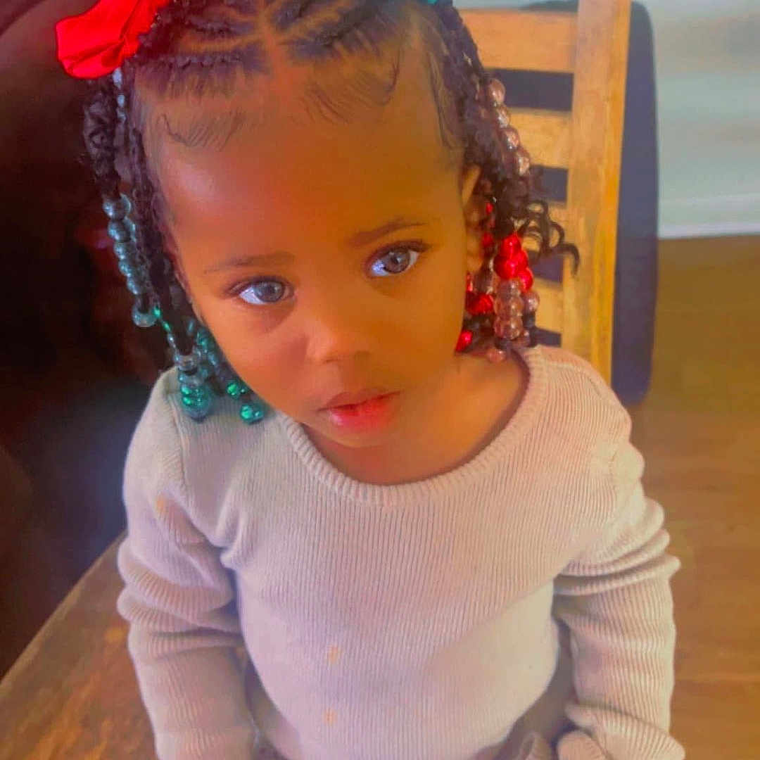 Taziyah joined the competition — help win amazing prizes! backpack, beige_sweater, braided_hair, child, curious_expression, cute, fashion, floor, girl, green_bow, hair_bows, home, indoor, patterned_pants, person, portrait, red_bow, sitting, wooden_chair, young_child