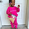 Kamani is registered to the contest to win money with this photo: toddler, child, girl, smile, braids, beads, pink_clothing, sweatshirt, pants, boots, cereal, plastic_bag, door, outdoor, standing, necklace, happy, person, casual, portrait