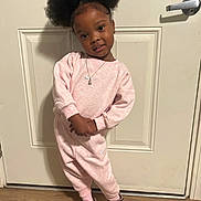 Kamani is registered to the contest to win money with this photo: child, girl, smile, pose, pink_clothing, tracksuit, nike_logo, hair_puffs, brown_slippers, door, wooden_floor, indoors, casual_wear, necklace, happy, cute, standing, portrait, young_child, face