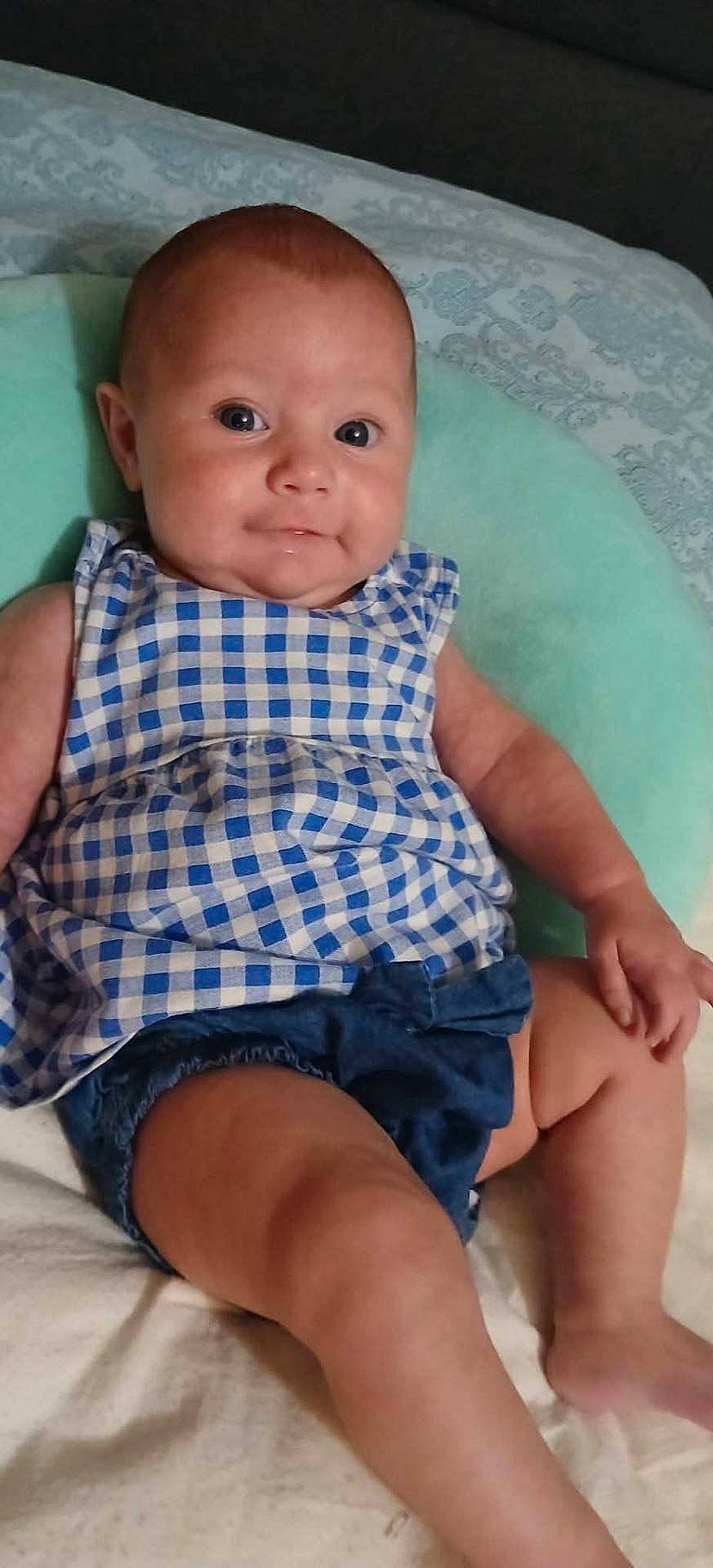 Samantha joined the competition — help win amazing prizes! arms, baby, blue_checkered_top, casual_clothing, child, cute, denim_shorts, eyes, face, indoors, infant, legs, person, portrait, relaxed, sitting, skin, smile, soft_surface, young