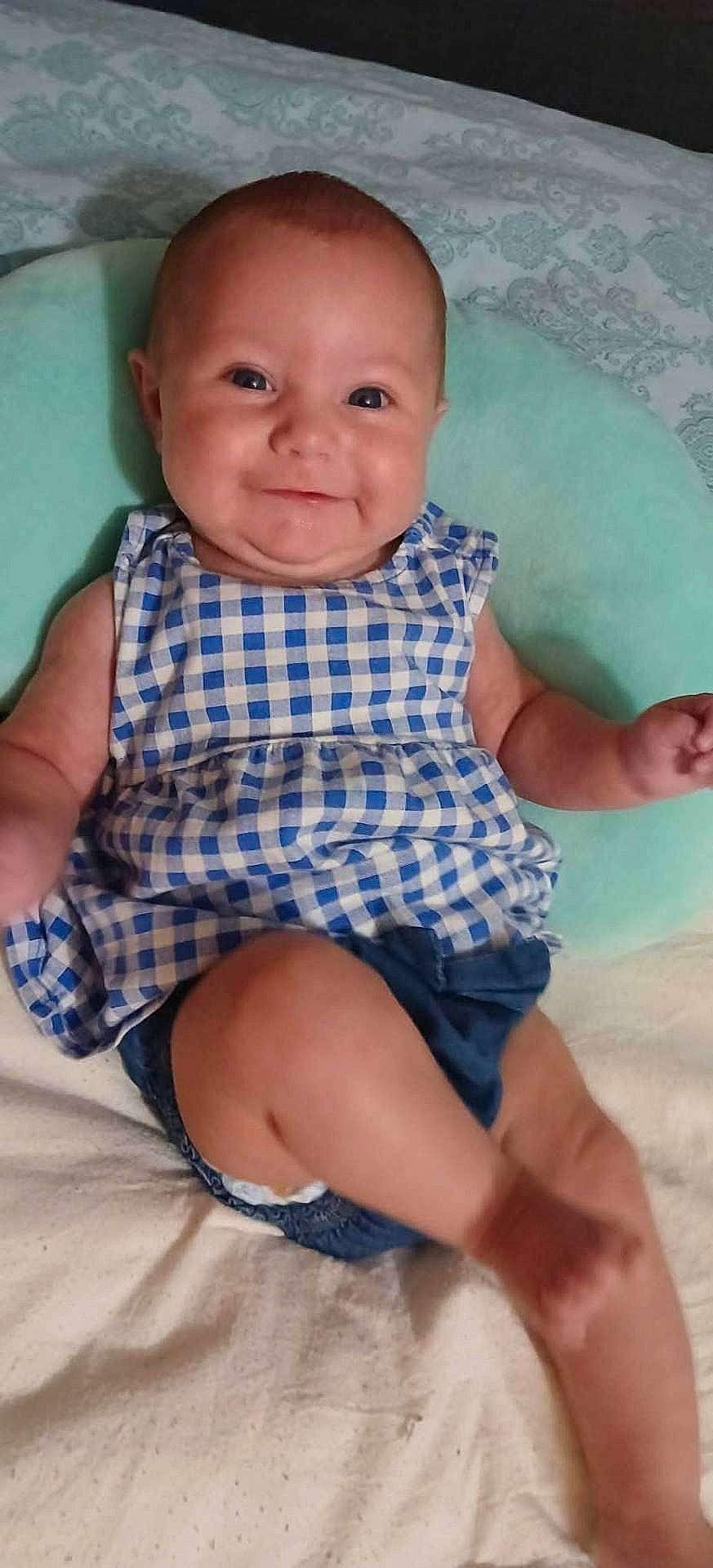 Samantha joined the competition — help win amazing prizes! arms, baby, blue_dress, checkered_pattern, child, clothing, comfortable, cushion, cute, face, happy, head, indoor, infant, legs, person, portrait, sitting, smiling, soft_surface