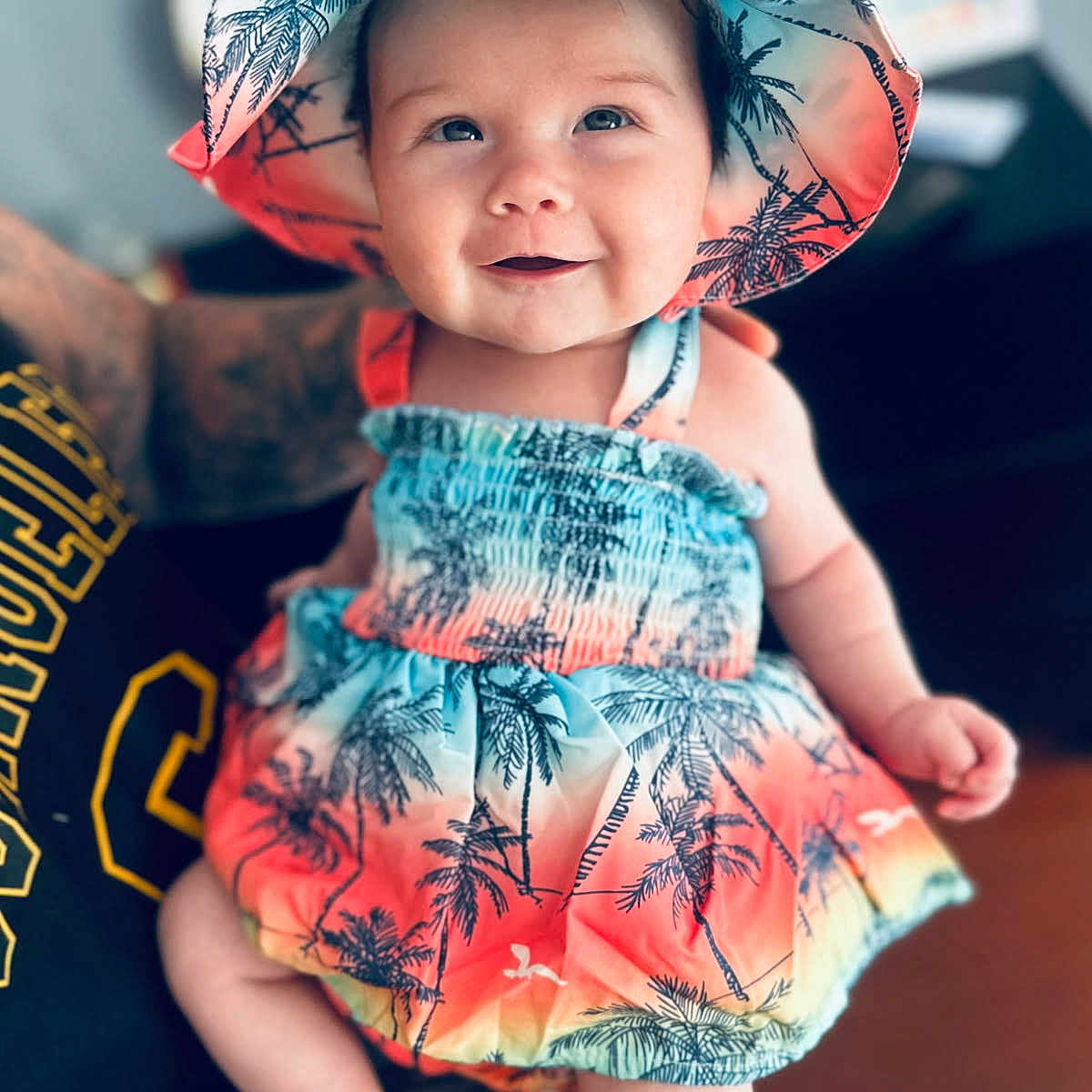 Lexi joined the competition — help win amazing prizes! baby, child, smiling, hat, colorful_clothing, tropical_pattern, toddler, portrait, indoor, person, cute, happy, summer_outfit, sitting, skin, face, headwear, bright, infant, closeup