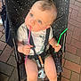 baby, stroller, child, blue_eyes, holding, pink_straw, green_straw, white_shirt, sitting, curious, outdoor, pavement, black_stroller, speckled_pattern, barefoot, summer_clothing, cute, infant, seatbelt, toy