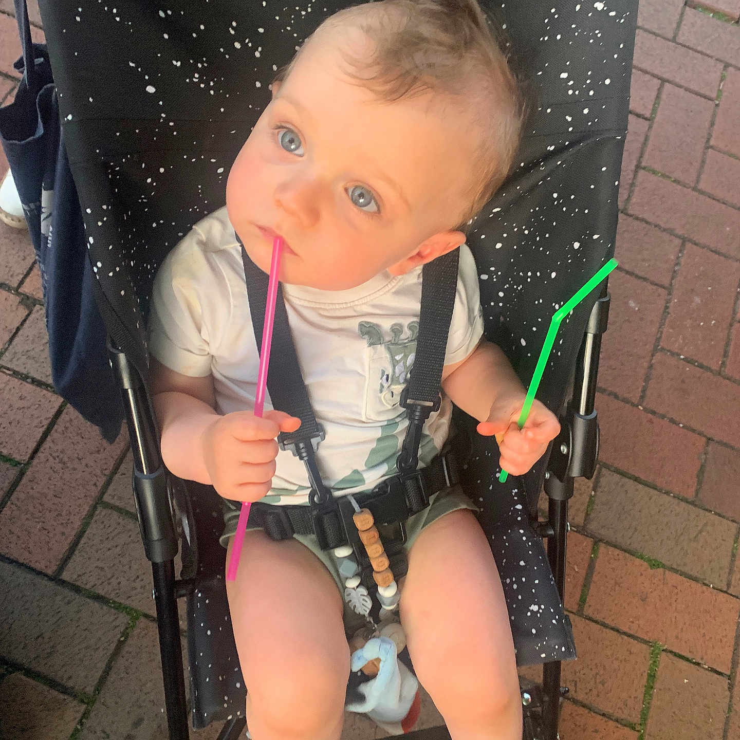 Arthur a rejoint le concours — aidez-le/la à gagner de superbes lots ! baby, barefoot, black_stroller, blue_eyes, child, curious, cute, green_straw, holding, infant, outdoor, pavement, pink_straw, seatbelt, sitting, speckled_pattern, stroller, summer_clothing, toy, white_shirt