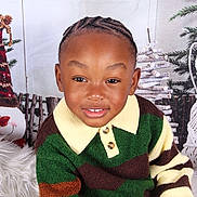 Amani joined the competition — help win amazing prizes! child, smiling, portrait, braided_hair, striped_sweater, green_sweater, brown_sweater, yellow_collar, holiday_decor, wooden_decoration, festive, indoor, cozy, seasonal, happy, cute, person, young_child, background, photography